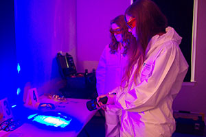 Fourth-year UOIT Forensic Science students Genevieve Belcour (left) and Chiara Ranalli (right) use fluorescent light to check specimen samples inside a lab at the Faculty of Science's Crime Scene House. 