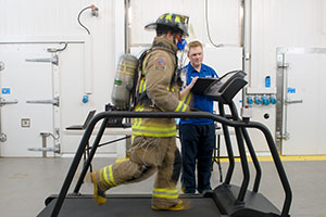 Michael Williams-Bell (right), PhD candidate (Applied Bioscience) conducts heat exertion test with a City of Toronto firefighter in one of ACE's climate chambers (temperature approximately 35 Celsius). 