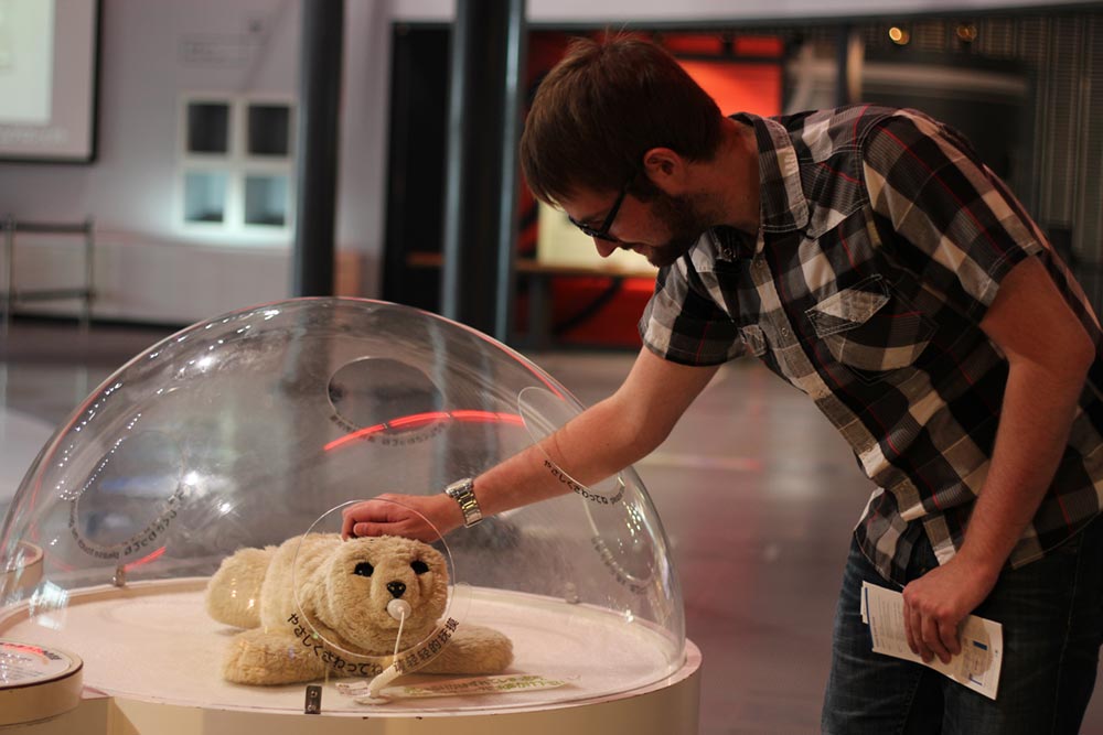 Nathan Gale petting a therapeutic robot named Paro at Miraikan: National Museum of Emerging Science and Innovation.