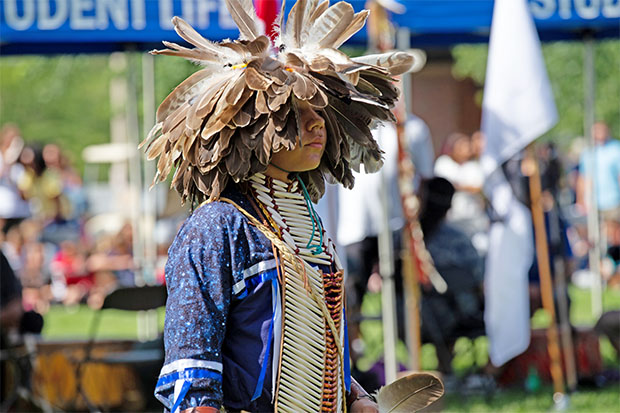 Xavier Anderson of the Eagle Clan in a traditional men's dance at the university's Mini Powwow (September 7, 2018). The colours of his regalia headdress are representative of the Golden Eagle. His regalia is the Woodland style.  