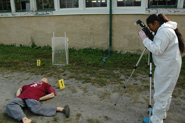 Third-year Ontario Tech University Forensic Science student investigating a mock suspected hit-and-run scenario involving documentation and analysis of glass fracture patterns and trace evidence. This mock scene is near the program's Crime Scene House on the university's former Windfields Farm lands.  