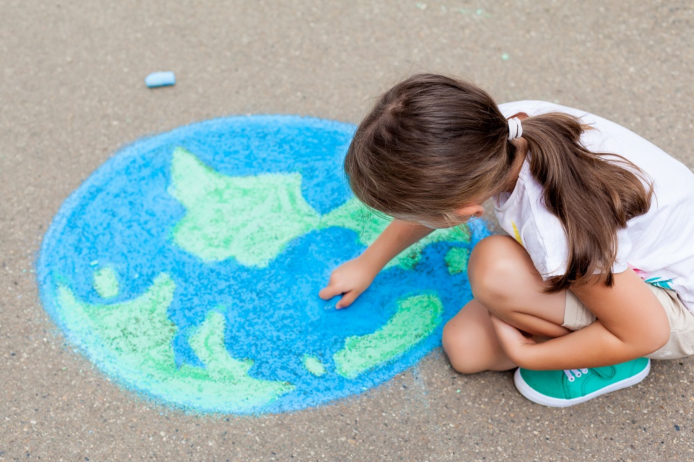 Child drawing globe on the ground with chalk