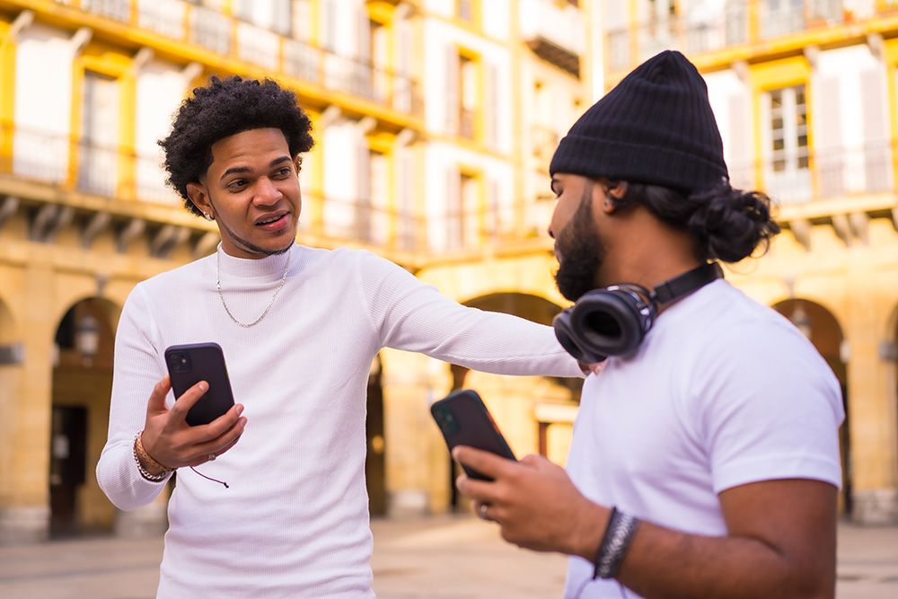 image of two friends meeting in the street, each holding iPhones, depicting technology.