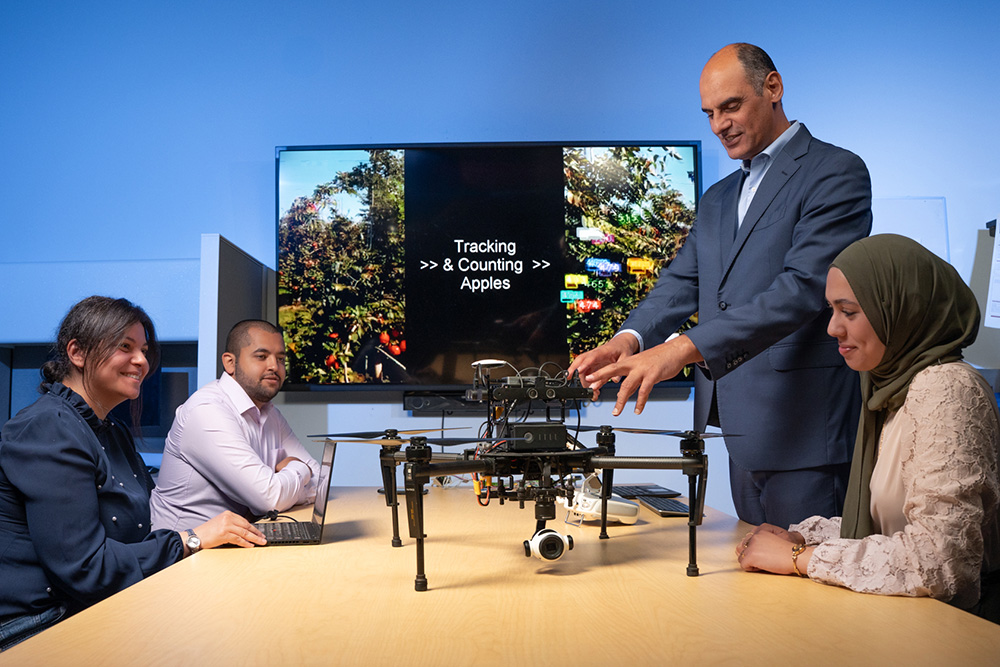 Dr. Khalid Elgazzar, Canada Research Chair in the Internet of Things (IoT) at Ontario Tech University (standing), speaks with members of his research group in the IoT Research Lab.