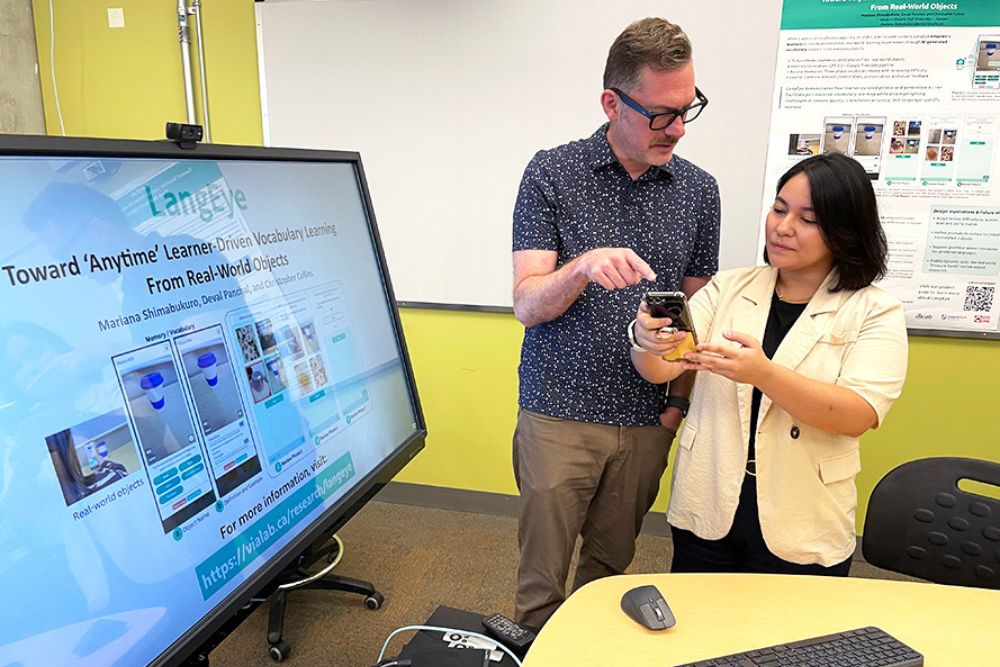 Dr. Christopher Collins, Professor (left) and Dr. Mariana Shimabukuro, Associate Teaching Professor, Faculty of Science, discuss the LangEye app in the Visualization for Information Analysis Laboratory at Ontario Tech University. 