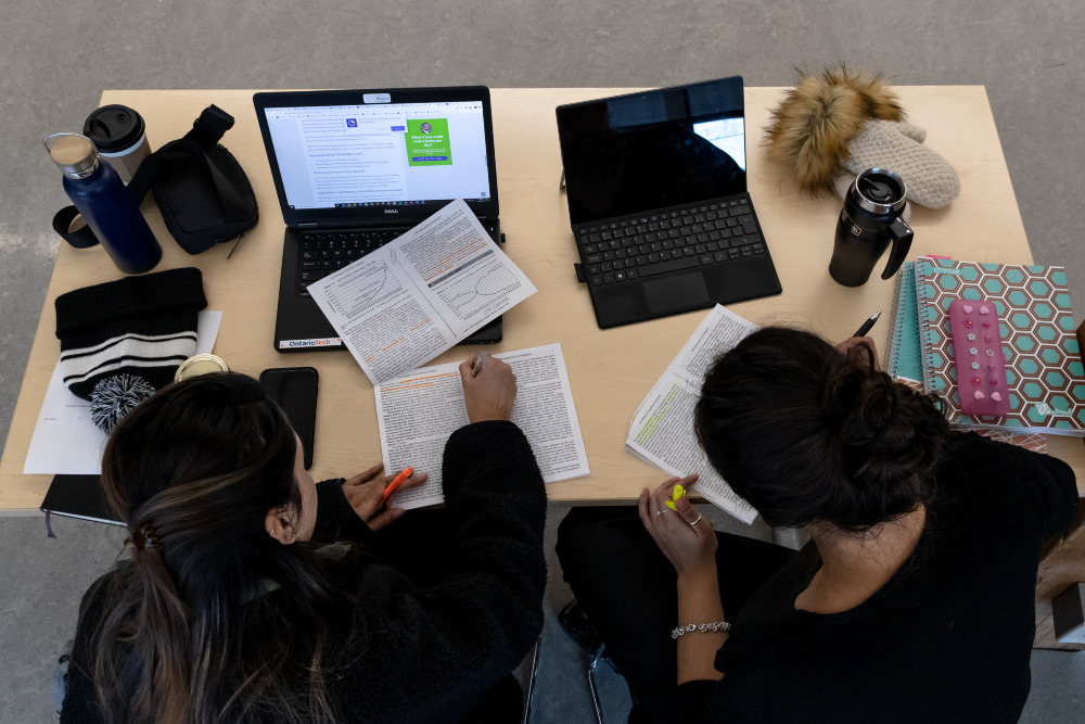Overhead image of students sitting at a table with their study materials and laptops open.