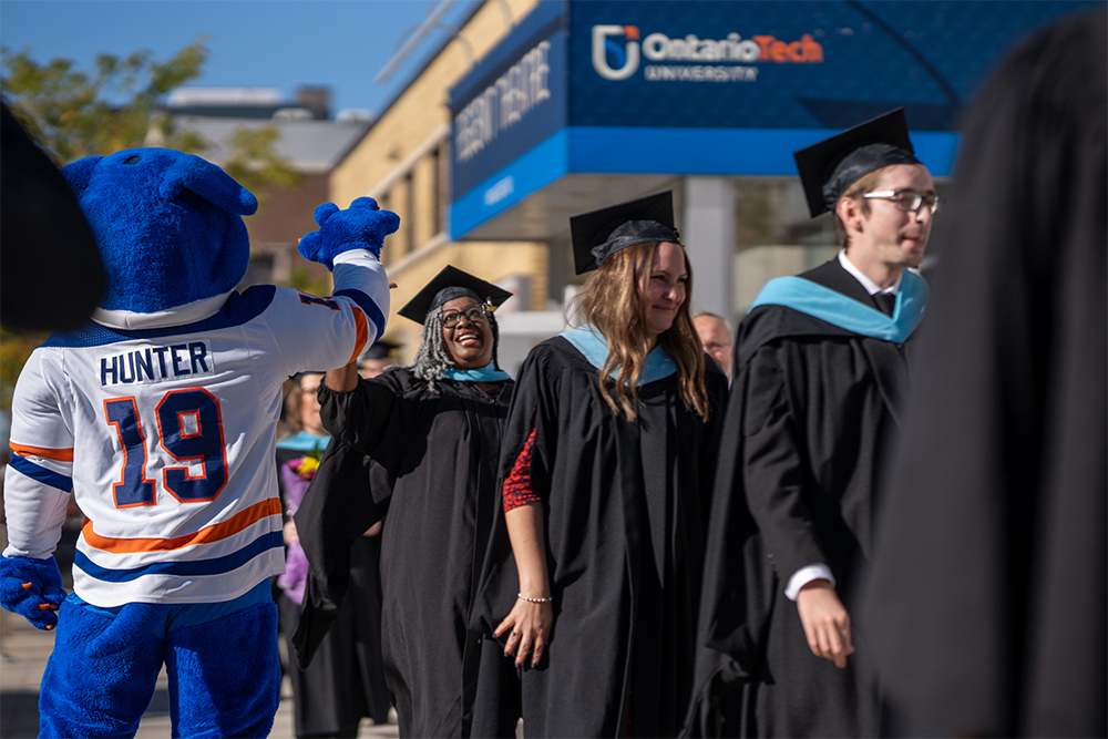 Graduate outside of Regent Theatre giving Hunter the Ridgeback a high-five at Convocation.